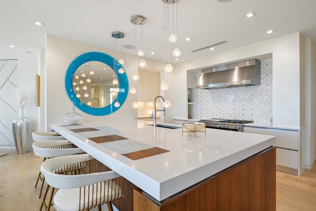 kitchen with sink, decorative light fixtures, wall chimney exhaust hood, stainless steel stove, and light wood-type flooring