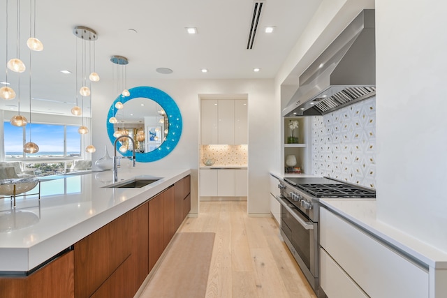 kitchen with high end stainless steel range, light wood-type flooring, decorative light fixtures, sink, and wall chimney range hood