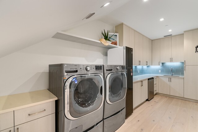 clothes washing area with washing machine and clothes dryer, light wood-type flooring, and sink