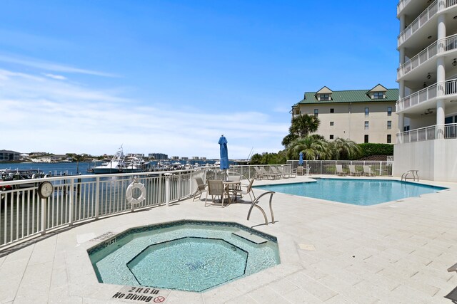 view of swimming pool featuring a patio, a water view, and a hot tub