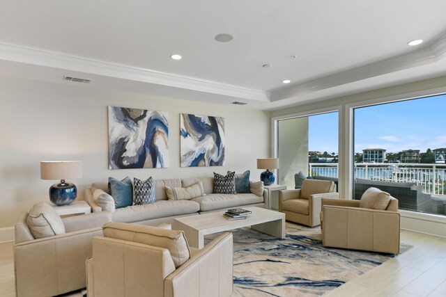 living room with ornamental molding, a water view, light hardwood / wood-style floors, and a raised ceiling