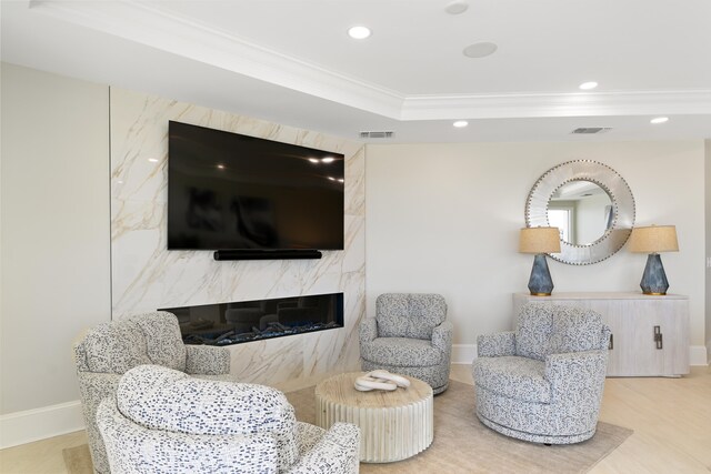 sitting room featuring wood-type flooring, a tray ceiling, a premium fireplace, and crown molding