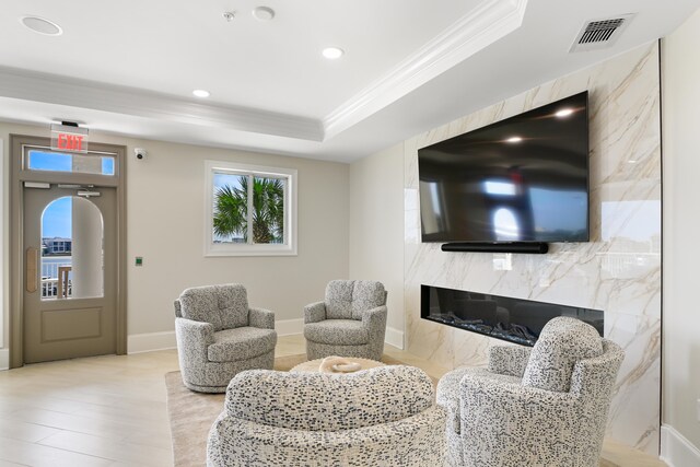 living room featuring a tray ceiling, a premium fireplace, light hardwood / wood-style floors, and crown molding