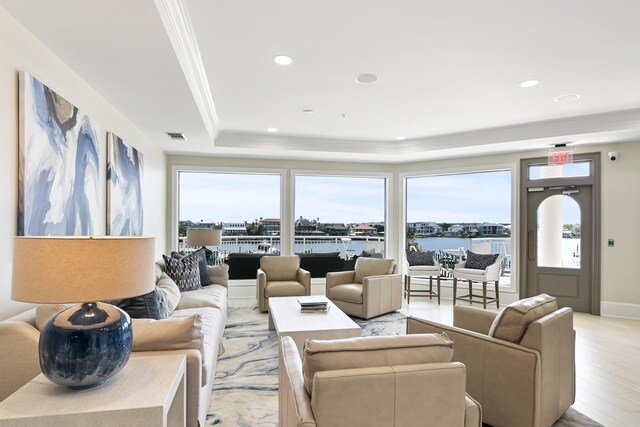 living room featuring light hardwood / wood-style flooring, a tray ceiling, and a water view