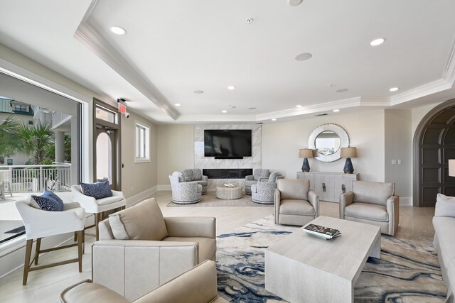 living room with ornamental molding, light wood-type flooring, a premium fireplace, and a raised ceiling