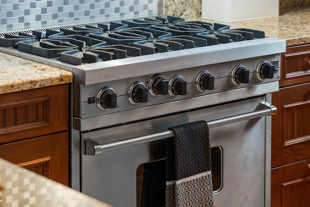 interior details with decorative backsplash, high end stainless steel range oven, and light stone countertops