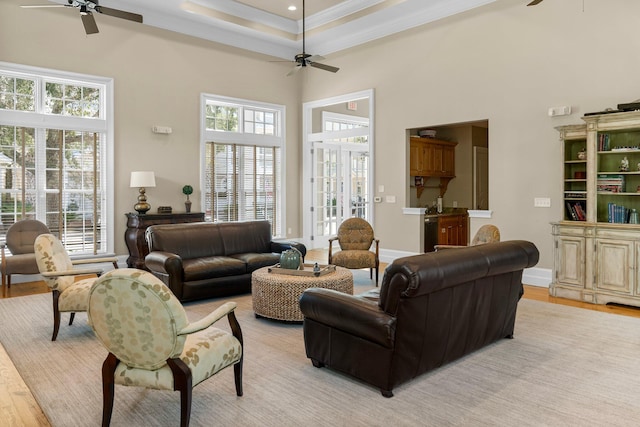 living room featuring light hardwood / wood-style floors, a towering ceiling, a raised ceiling, crown molding, and ceiling fan