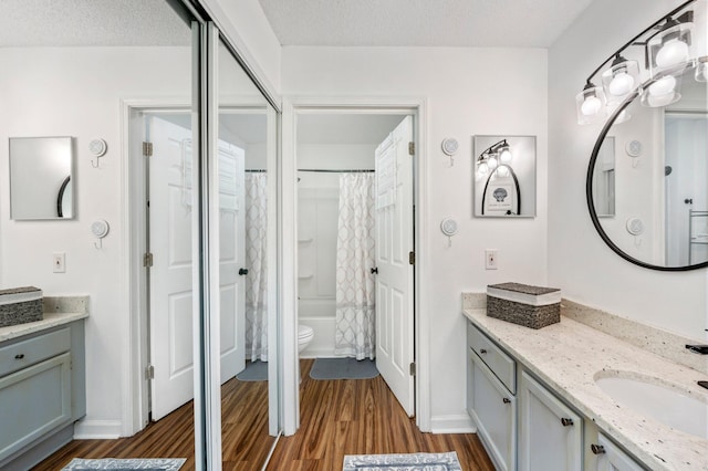 full bathroom with wood-type flooring, shower / bath combo, a textured ceiling, vanity, and toilet