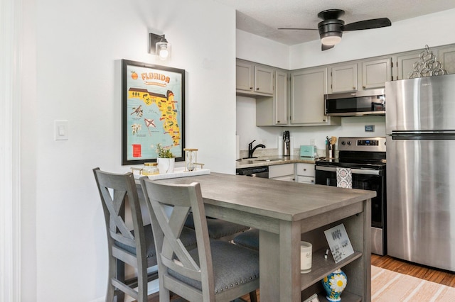 kitchen with light wood-type flooring, a textured ceiling, sink, stainless steel appliances, and ceiling fan