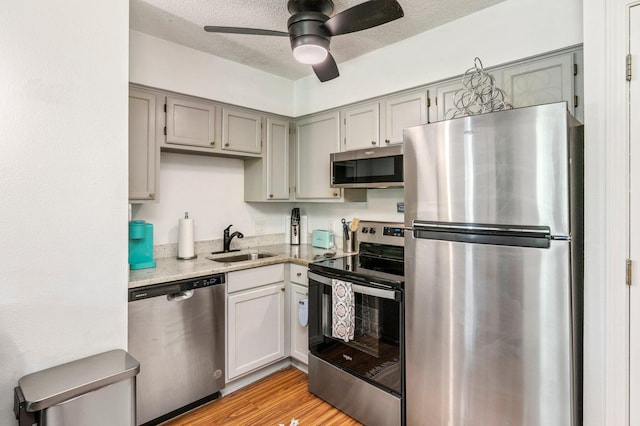 kitchen with ceiling fan, sink, a textured ceiling, stainless steel appliances, and light wood-type flooring