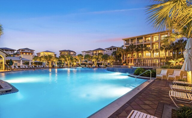 pool at dusk featuring pool water feature and a patio