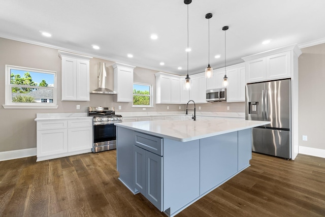 kitchen featuring appliances with stainless steel finishes, white cabinetry, light stone countertops, decorative light fixtures, and wall chimney exhaust hood