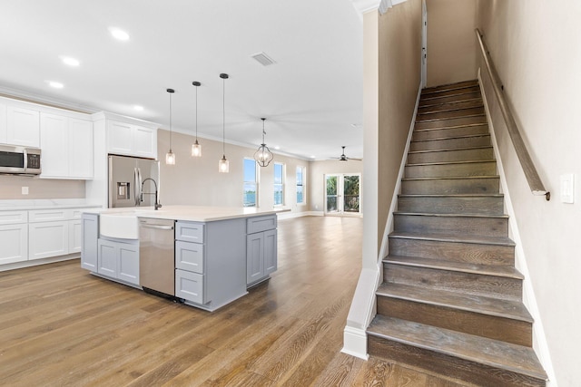 kitchen featuring light hardwood / wood-style flooring, appliances with stainless steel finishes, an island with sink, white cabinets, and decorative light fixtures