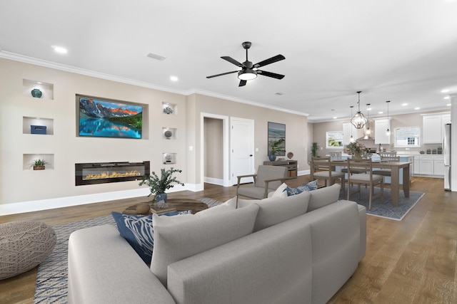 living room with baseboards, ceiling fan, crown molding, wood finished floors, and a glass covered fireplace