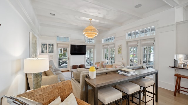 living room featuring a notable chandelier, beamed ceiling, french doors, and light hardwood / wood-style flooring