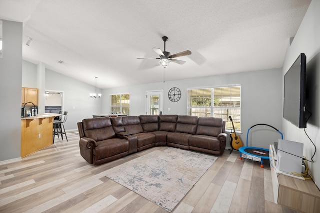 living room with a textured ceiling, ceiling fan with notable chandelier, light hardwood / wood-style flooring, and vaulted ceiling