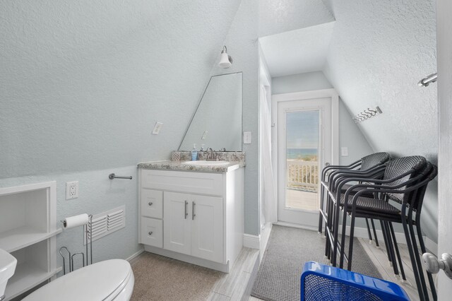 bathroom featuring a textured ceiling, vaulted ceiling, hardwood / wood-style floors, vanity, and toilet