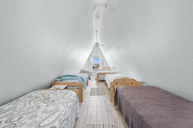 bedroom with ceiling fan, a textured ceiling, light wood-type flooring, and lofted ceiling