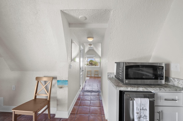 hallway featuring dark tile patterned flooring, a textured ceiling, and lofted ceiling