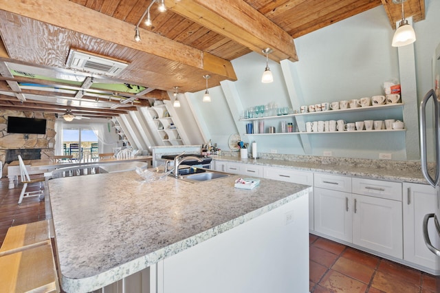 kitchen featuring a stone fireplace, white cabinets, hanging light fixtures, and sink