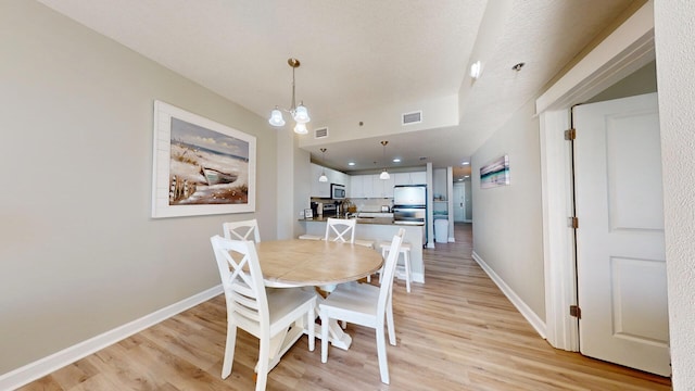 dining space featuring a textured ceiling, light hardwood / wood-style floors, and a chandelier