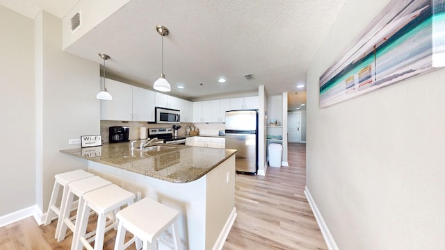 kitchen featuring pendant lighting, white cabinets, kitchen peninsula, stainless steel appliances, and light wood-type flooring