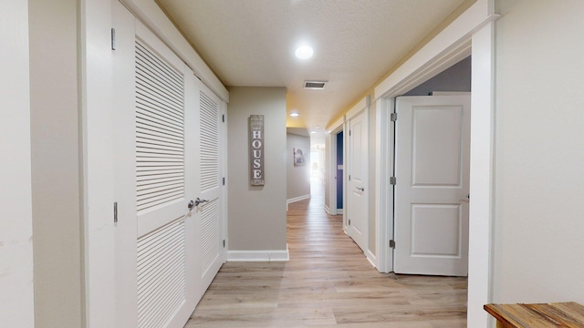 corridor with a textured ceiling and light hardwood / wood-style flooring