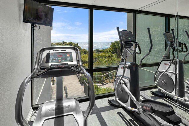 gym featuring a wall of windows, a water view, and a textured wall