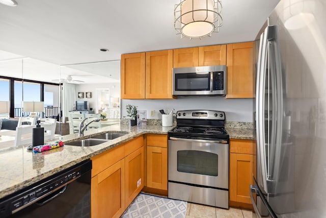 kitchen featuring a sink, stainless steel appliances, a ceiling fan, light stone counters, and open floor plan