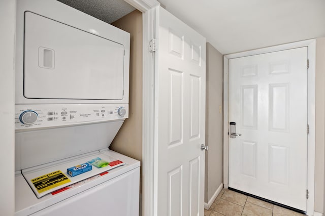 clothes washing area featuring light tile patterned flooring, stacked washer and clothes dryer, laundry area, and baseboards