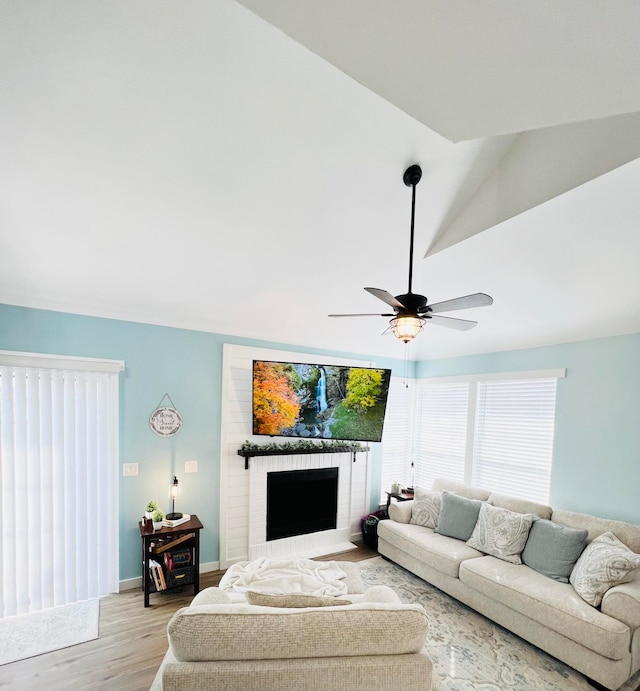 living room featuring a brick fireplace, light hardwood / wood-style flooring, lofted ceiling, and ceiling fan