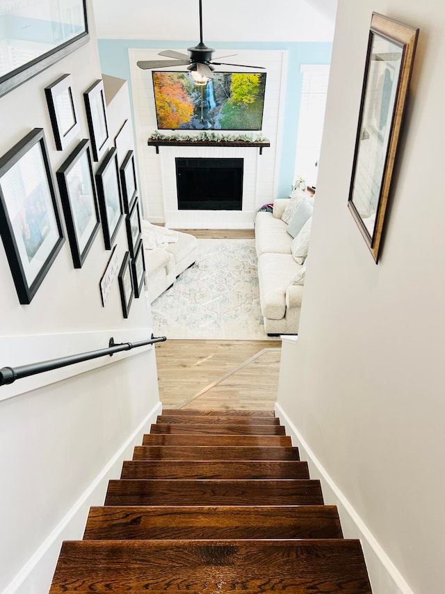 staircase featuring a brick fireplace, ceiling fan, and hardwood / wood-style floors