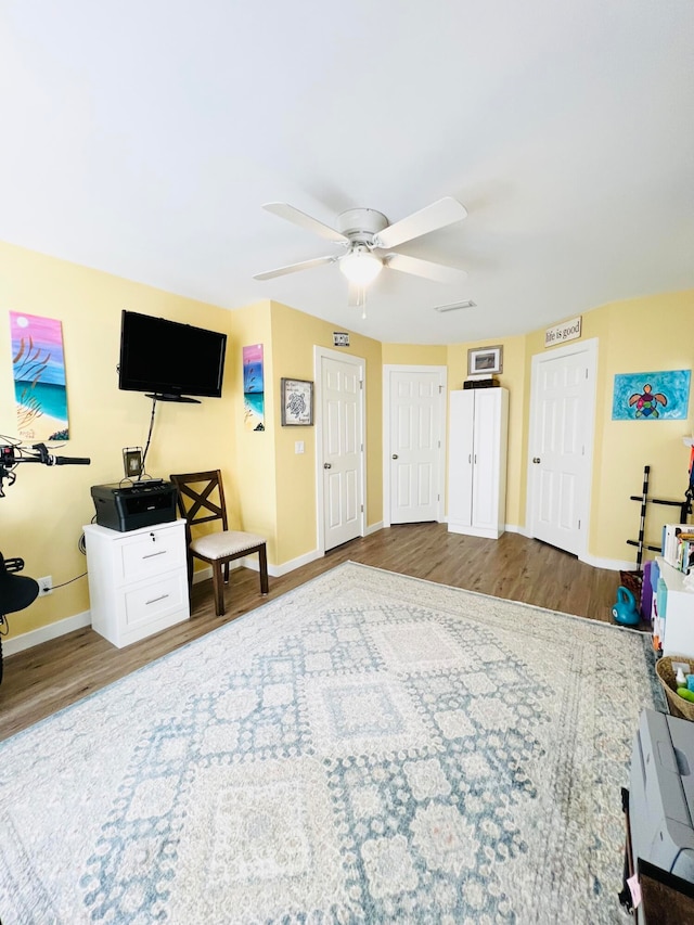 interior space with wood-type flooring, multiple closets, and ceiling fan