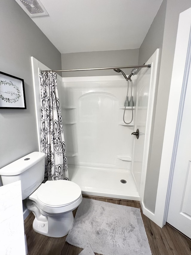 bathroom with wood-type flooring, a shower with curtain, and toilet