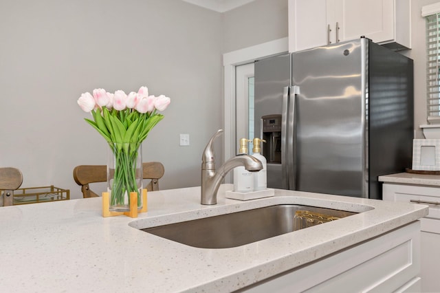 kitchen with white cabinets, light stone counters, sink, and stainless steel fridge