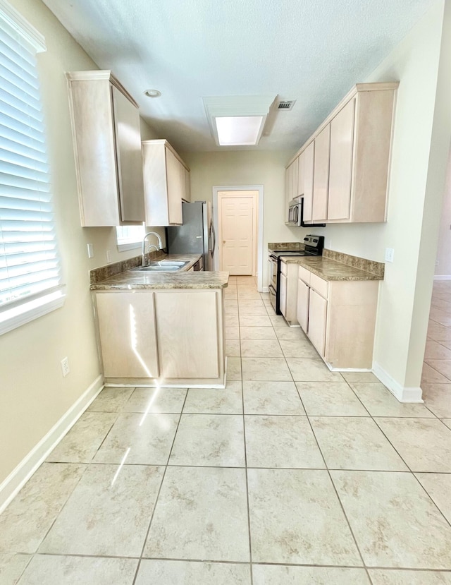 kitchen with light tile patterned floors, a skylight, stainless steel appliances, and sink