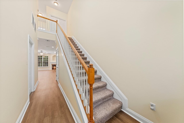 stairway with a towering ceiling, ceiling fan, and hardwood / wood-style flooring