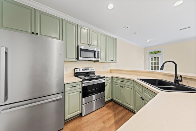 kitchen with stainless steel appliances, crown molding, light hardwood / wood-style flooring, sink, and green cabinets