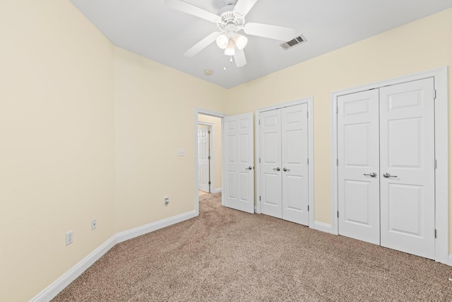 unfurnished bedroom with light carpet, ceiling fan, and multiple closets