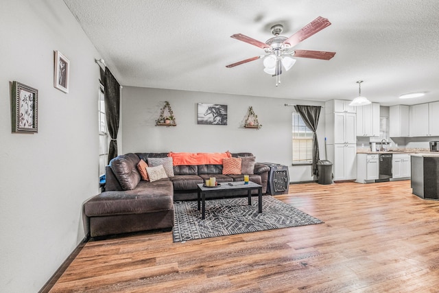 living room with light wood-type flooring, a textured ceiling, sink, and ceiling fan