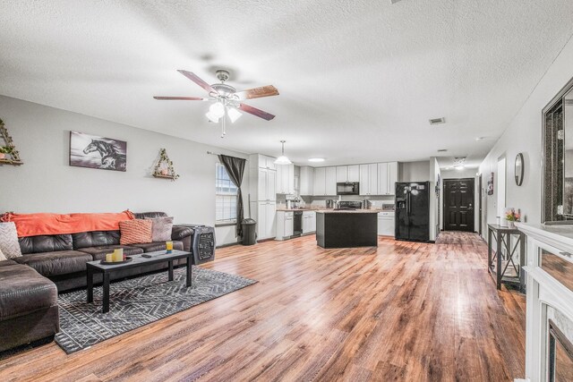 living room featuring ceiling fan, a textured ceiling, and light hardwood / wood-style floors