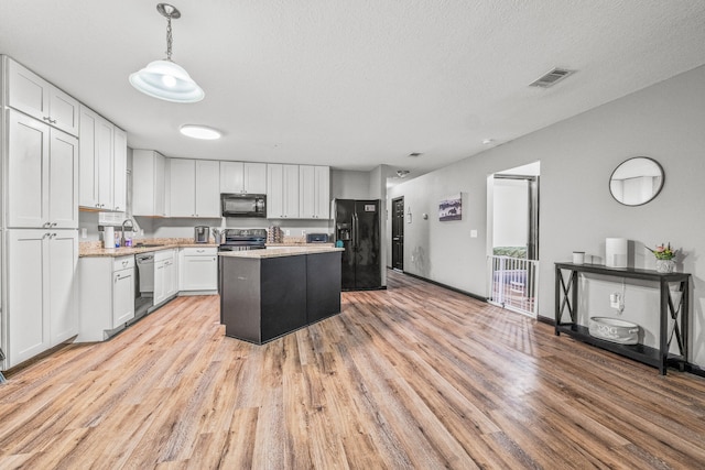 kitchen featuring light wood-type flooring, a center island, white cabinets, hanging light fixtures, and black appliances