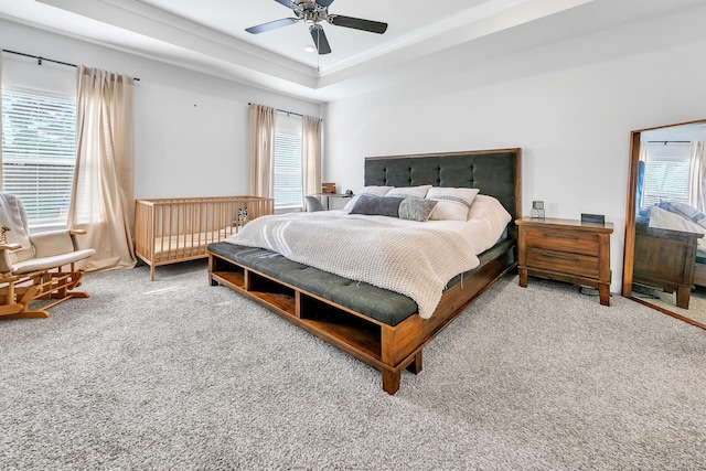 carpeted bedroom featuring a raised ceiling, multiple windows, and ceiling fan