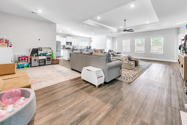 living room featuring ceiling fan, a raised ceiling, and wood-type flooring