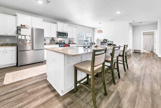 kitchen with appliances with stainless steel finishes, a kitchen island with sink, and white cabinetry