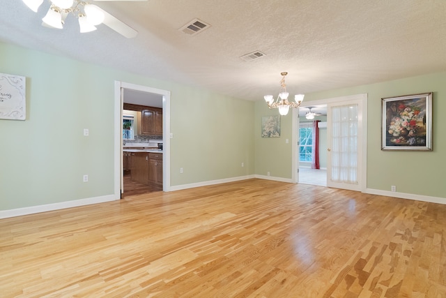 empty room featuring french doors, ceiling fan with notable chandelier, a textured ceiling, and light hardwood / wood-style flooring