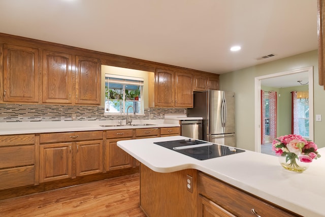 kitchen with stainless steel appliances, light wood-type flooring, sink, and tasteful backsplash