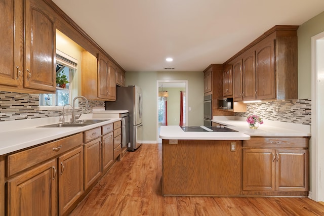 kitchen with appliances with stainless steel finishes, sink, light hardwood / wood-style floors, and tasteful backsplash