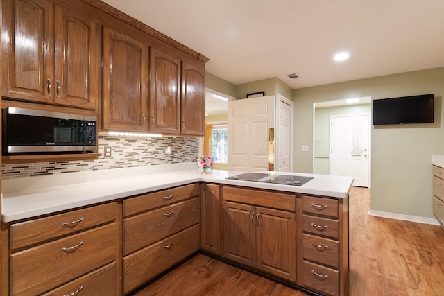 kitchen featuring kitchen peninsula, light hardwood / wood-style floors, decorative backsplash, and black electric stovetop