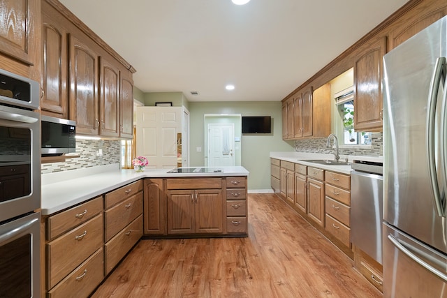 kitchen featuring light wood-type flooring, decorative backsplash, sink, kitchen peninsula, and appliances with stainless steel finishes